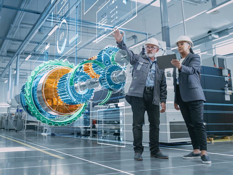 Two engineers in hard hats stand in a high-tech manufacturing facility, examining a holographic projection of mechanical gears and components. One holds a tablet while the other points at the hologram.