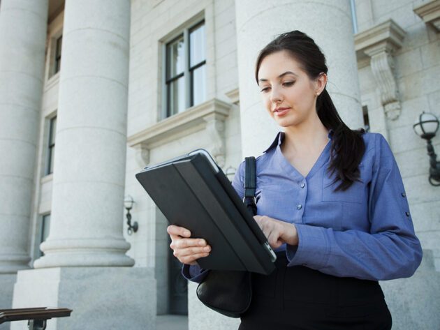 Woman using a tablet outside a building with large columns.