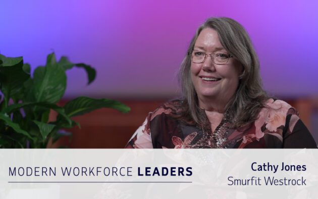A woman with long gray hair and glasses smiles during an interview, seated next to a green plant. Text reads: "MODERN WORKFORCE LEADERS. Cathy Jones, Smurfit Westrock shares insights on workforce management software.