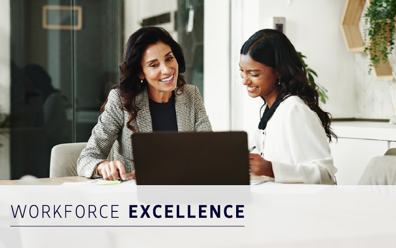 Two women sit at a desk, smiling and looking at a laptop. The text “Workforce Excellence” appears across the bottom of the image.