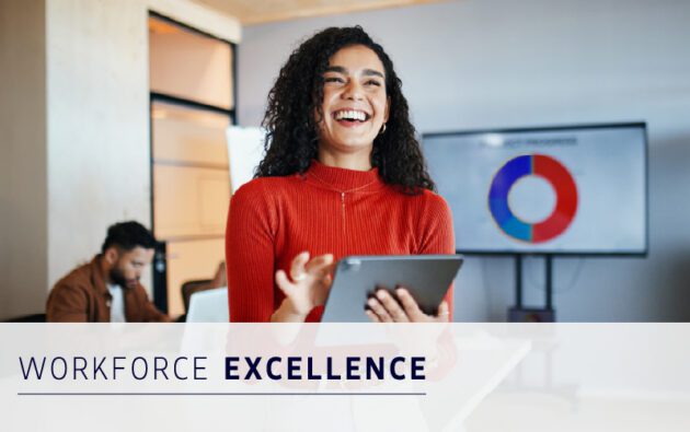 A woman holding a tablet smiles in an office; a man works at a desk in the background, and a pie chart is displayed on a screen. Text reads "Workforce Excellence.