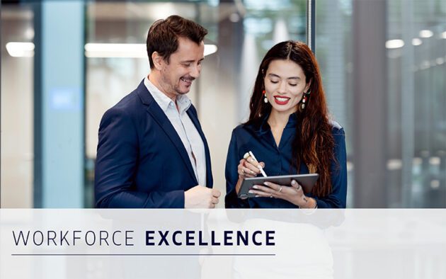 Two professionals in business attire stand together, smiling as the woman writes on a digital tablet. The text "Workforce Excellence" appears at the bottom of the image.