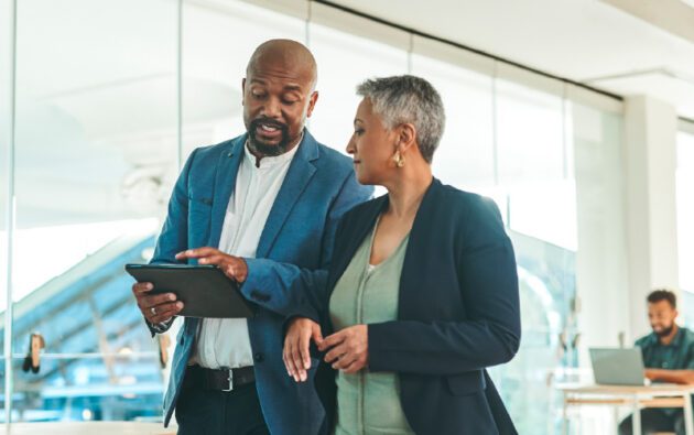 A man and a woman in business attire looking at a tablet together in an office.