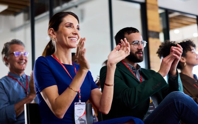 A diverse group of people sitting in a conference room, smiling and clapping.